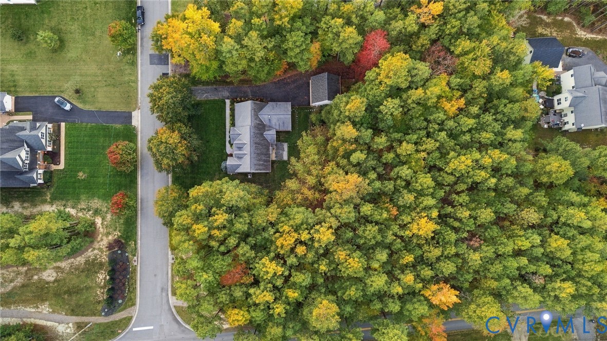 Aerial perspective of a residential property featuring a paved driveway, detached storage structure, multi-pitch roofline, and expansive wooded grounds