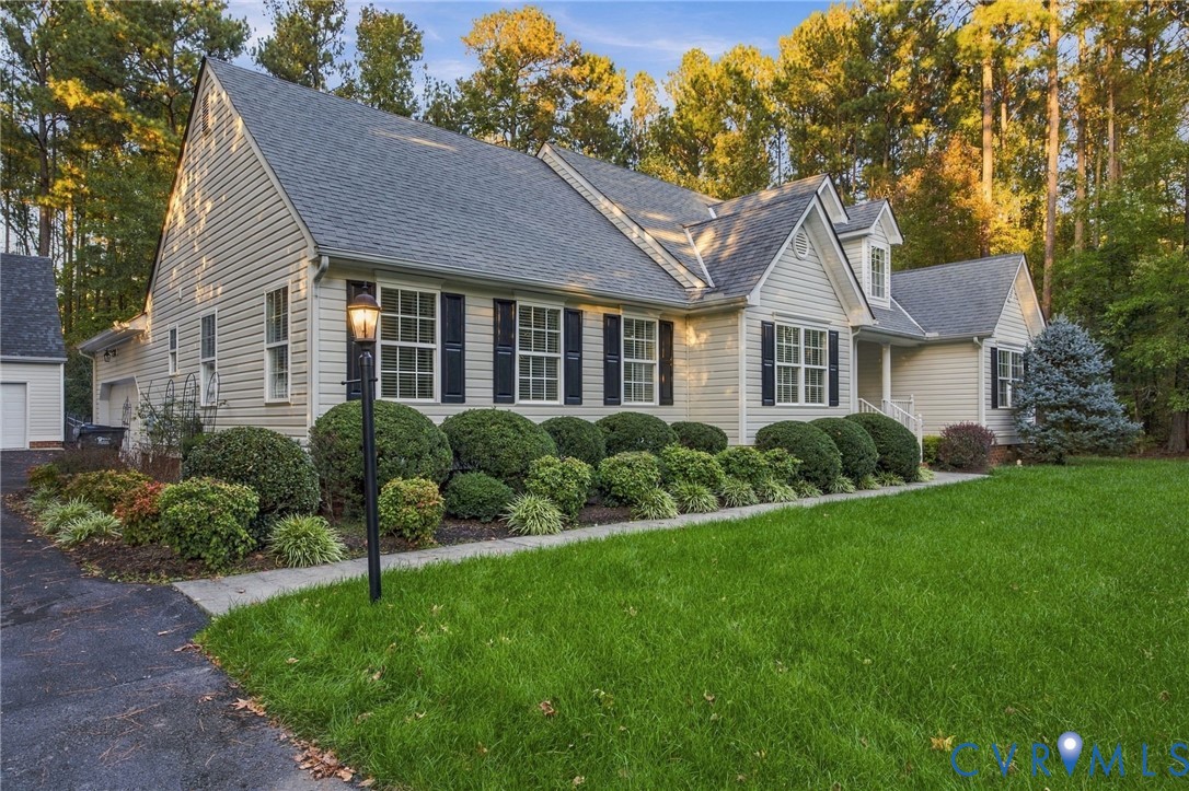 Traditional siding exterior featuring a gable roofline, multi-pane windows with dark shutters, and mature professional landscaping