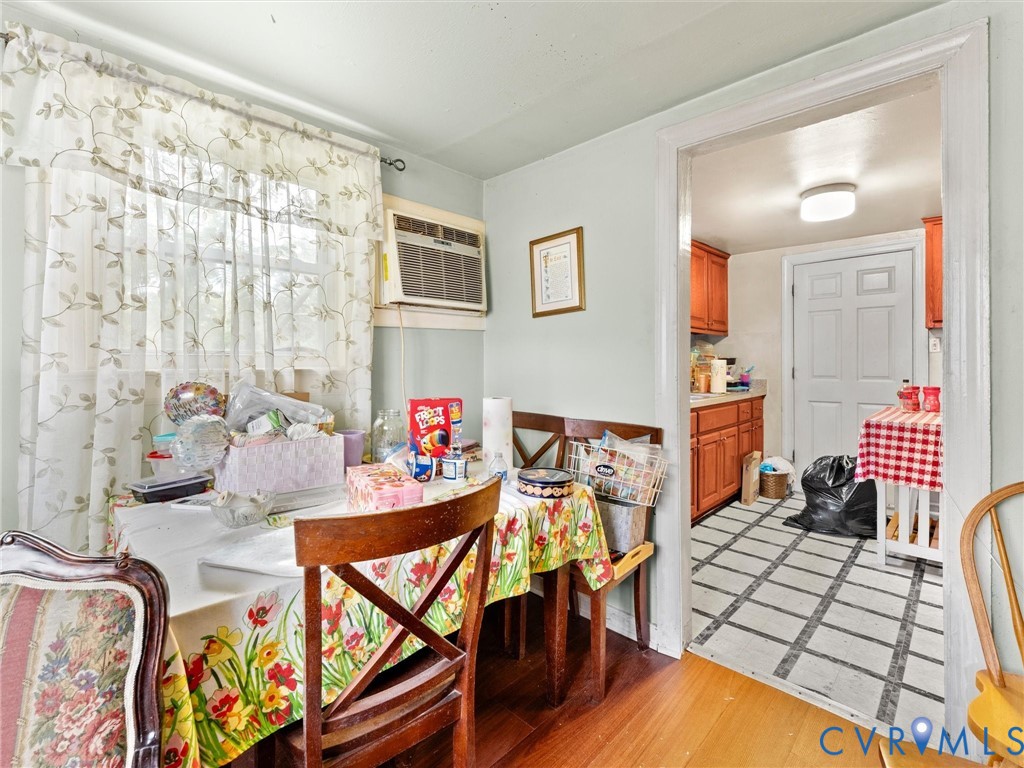 Dining area featuring wood-finish flooring and a window with trim, complemented by an opening to a kitchen area with tile flooring and wood cabinetry