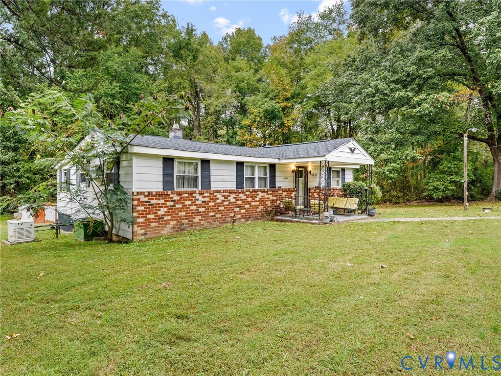 Ranch-style exterior featuring a brick and white siding facade, asphalt shingle roof, covered front porch with iron supports, and a large lot with mature trees