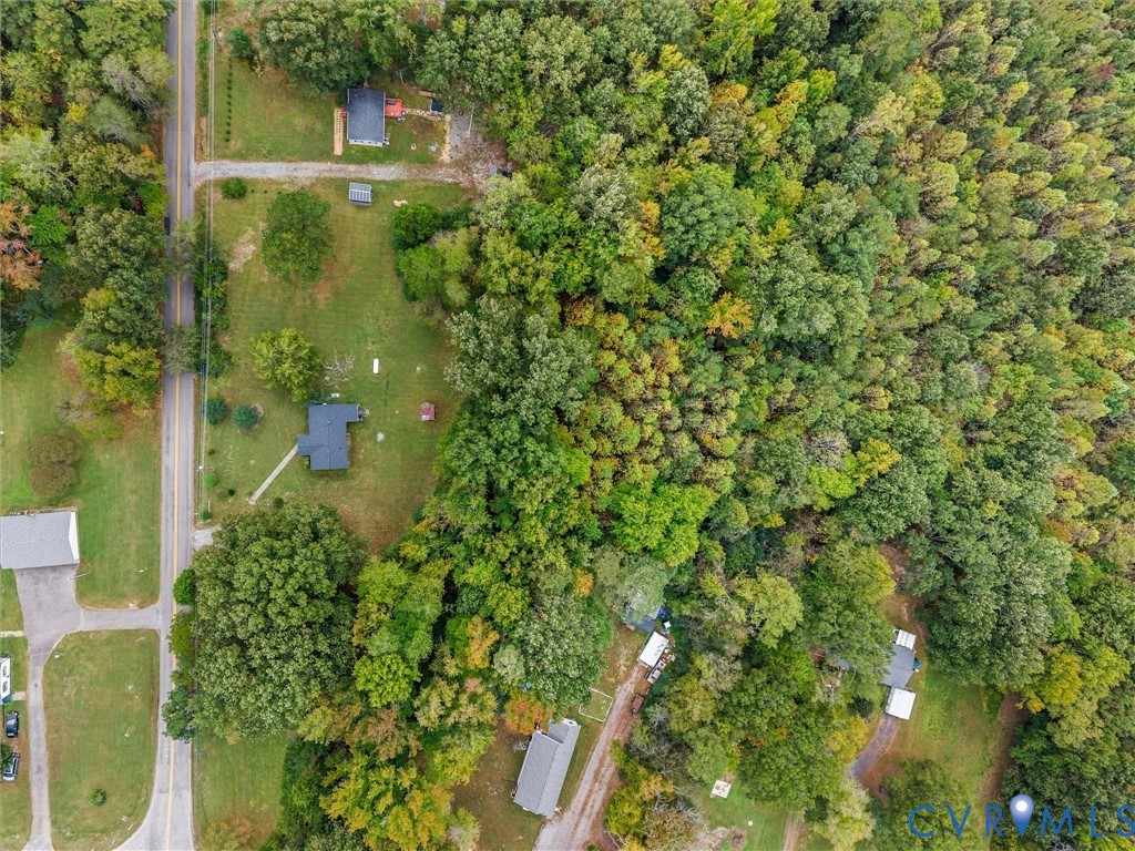 Aerial view of expansive lot featuring open grassy grounds, mature woodland coverage, and direct paved road access