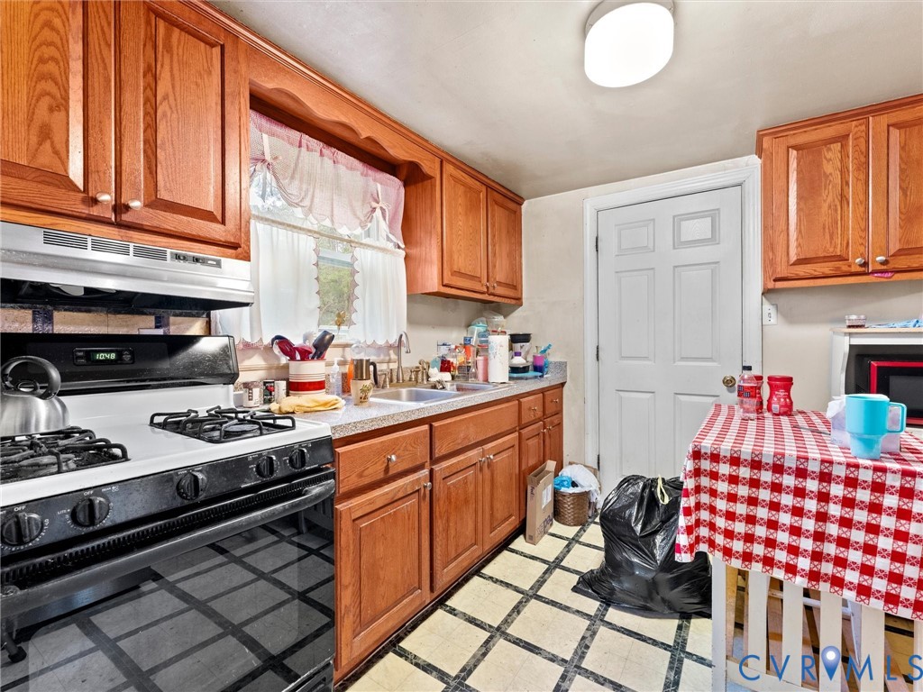 Kitchen featuring natural wood cabinetry, gas range with an overhead exhaust hood, stainless steel sink, and grid-patterned tile flooring