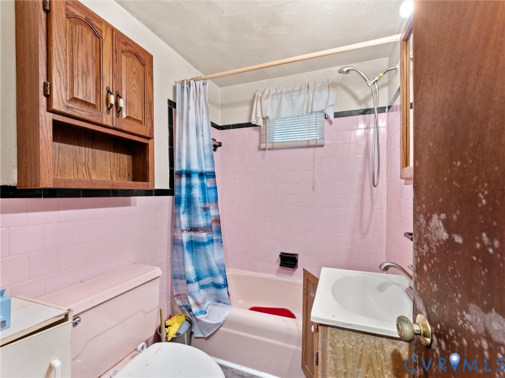 Bathroom featuring pink wall tiling with black accent trim, wood-finish wall-mounted cabinetry, integrated bathtub, and a pedestal sink