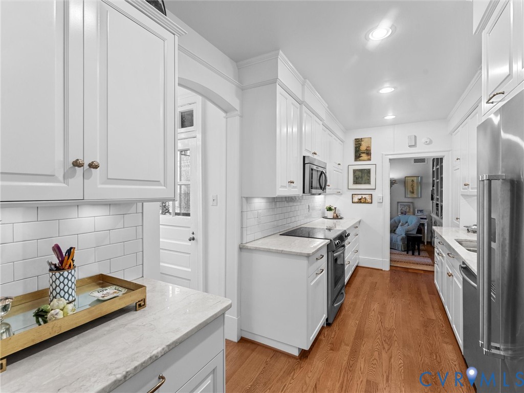 Kitchen featuring white cabinetry, stone countertops, subway tile backsplash, stainless steel appliances, and wood-finish flooring