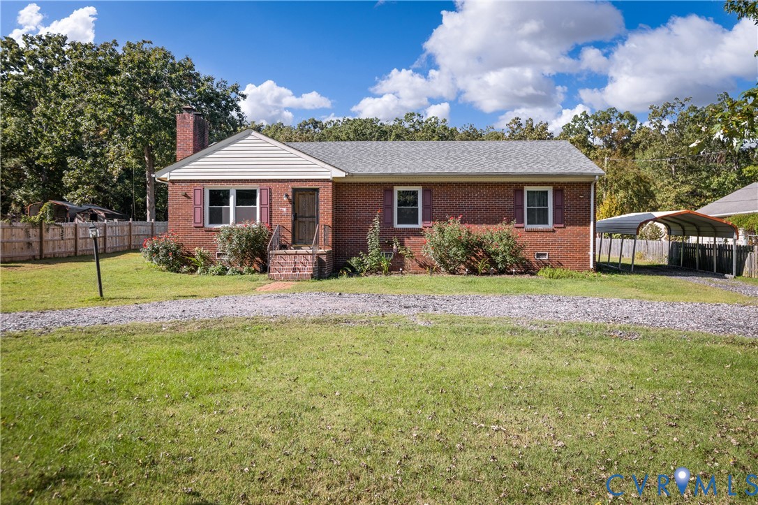 Brick exterior residence featuring a gable roof, exterior chimney, covered carport, and a gravel driveway