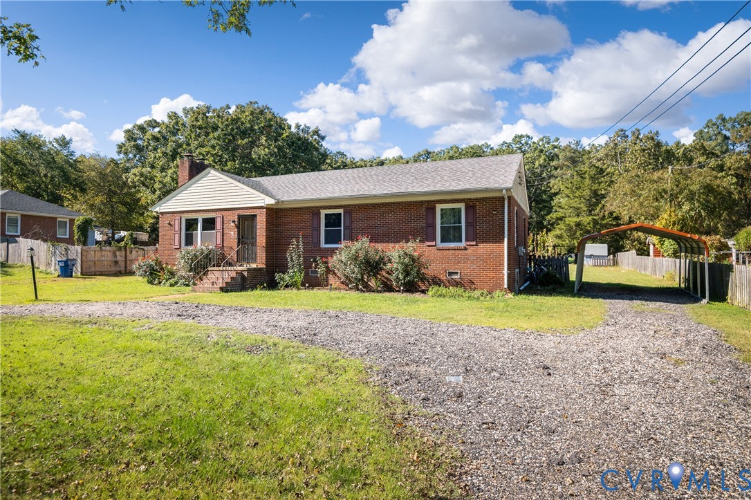 Brick exterior residence featuring a gabled roofline, decorative window shutters, a gravel driveway, and a detached metal carport
