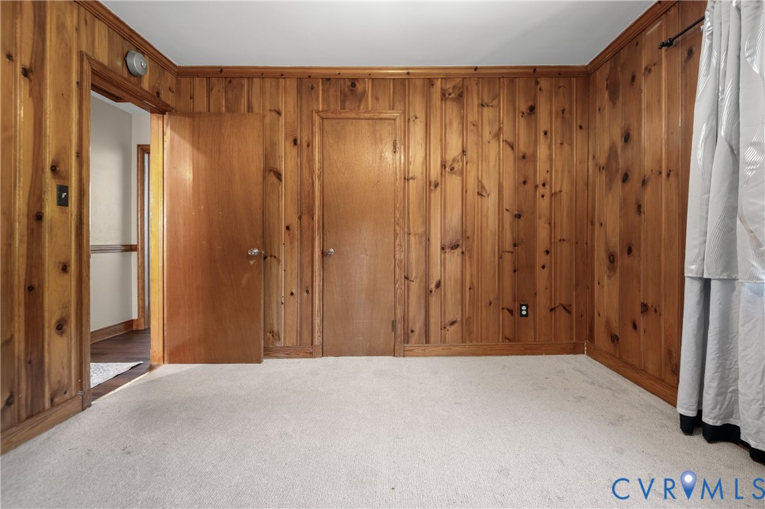 Room featuring floor-to-ceiling wood paneling, solid wood interior doors, and neutral carpeting