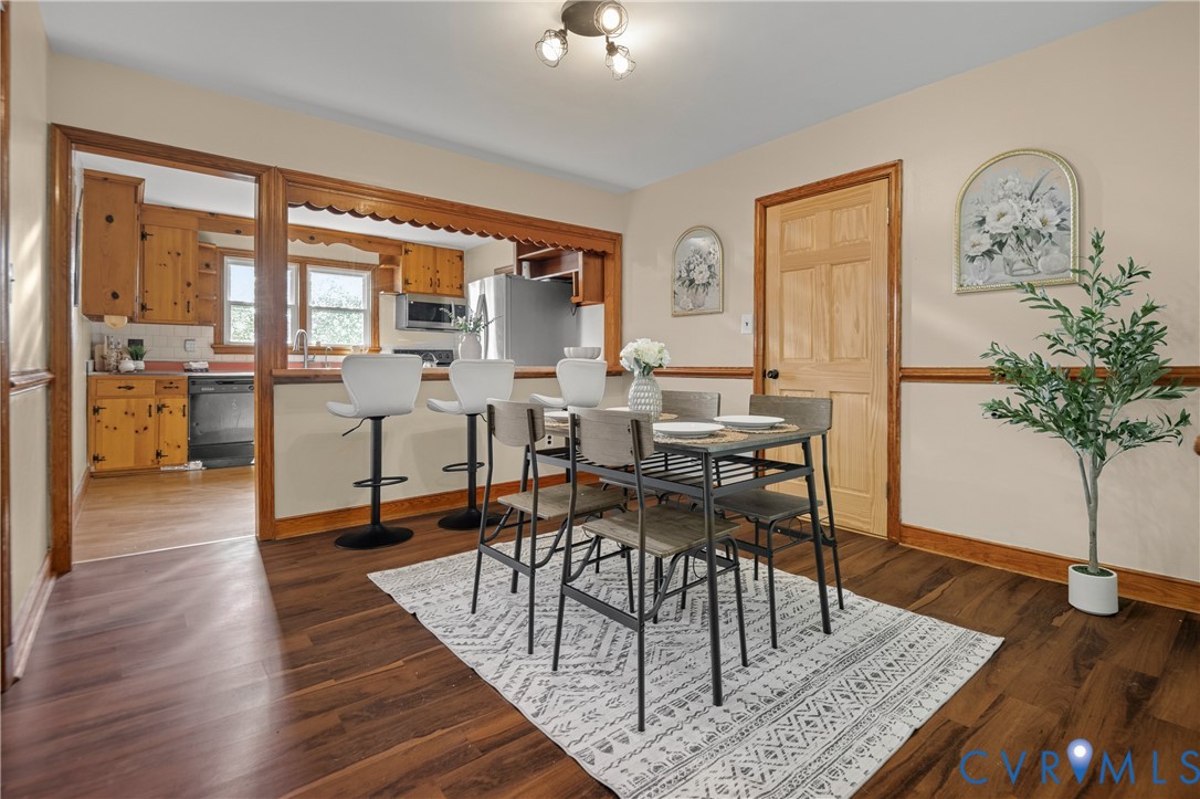 Dining area featuring wood-finish flooring, a decorative scalloped pass-through opening, natural wood trim, a six-panel solid wood door, and three-light track fixture Dining area featuring wood-finish flooring, a decorative scalloped pass-through opening, natural wood trim, a six-panel solid wood door, and three-light track fixture