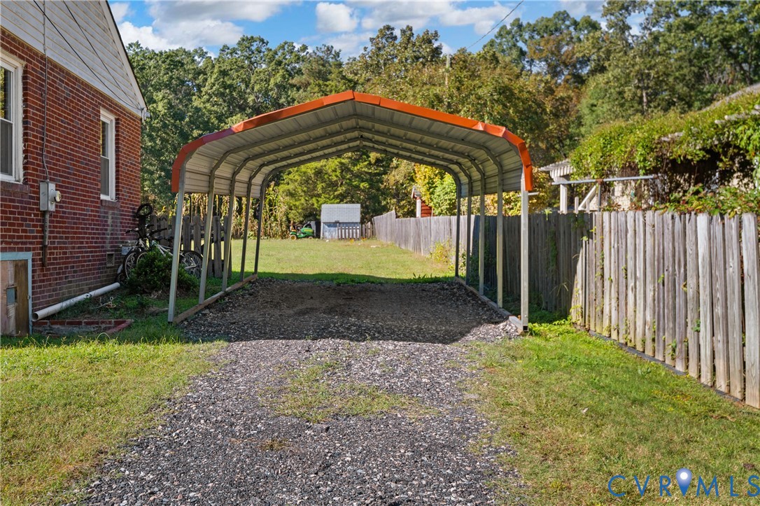 Detached metal carport featuring a gravel-surfaced parking area, red brick exterior walling, and fenced perimeter