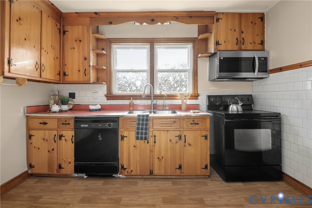 Kitchen featuring knotty wood cabinetry, white subway tile backsplash, dual-basin stainless steel sink with pull-down faucet, and black built-in appliances
