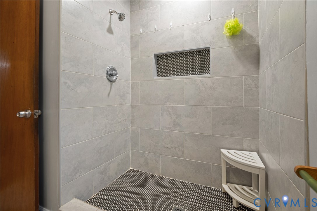 Walk-in shower featuring large-format light gray wall tile, contrasting circular mosaic floor tile, built-in wall niche, and polished chrome shower fixture