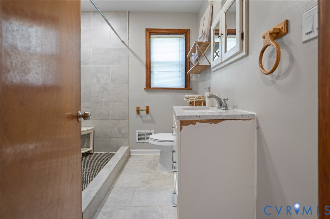 Bathroom featuring large-format tile flooring, walk-in shower with light-toned wall tile, white vanity with stone-composite countertop, and wall-mounted medicine cabinet