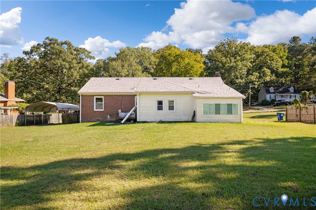 Expansive backyard featuring a large grass lawn, mature trees, brick and siding exterior, and a detached metal carport