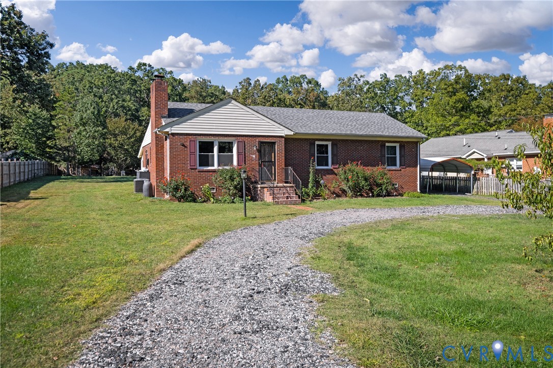 Brick exterior residence featuring an attached exterior chimney, a gravel driveway, and a detached carport structure