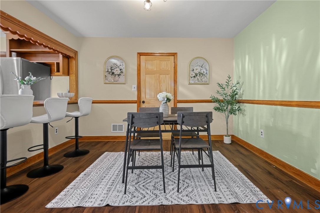 Dining area featuring wood-finish flooring, wood-toned chair rail molding, a pass-through opening with decorative wood trim, and a six-panel wood door Dining area featuring wood-finish flooring, wood-toned chair rail molding, a pass-through opening with decorative wood trim, and a six-panel wood door