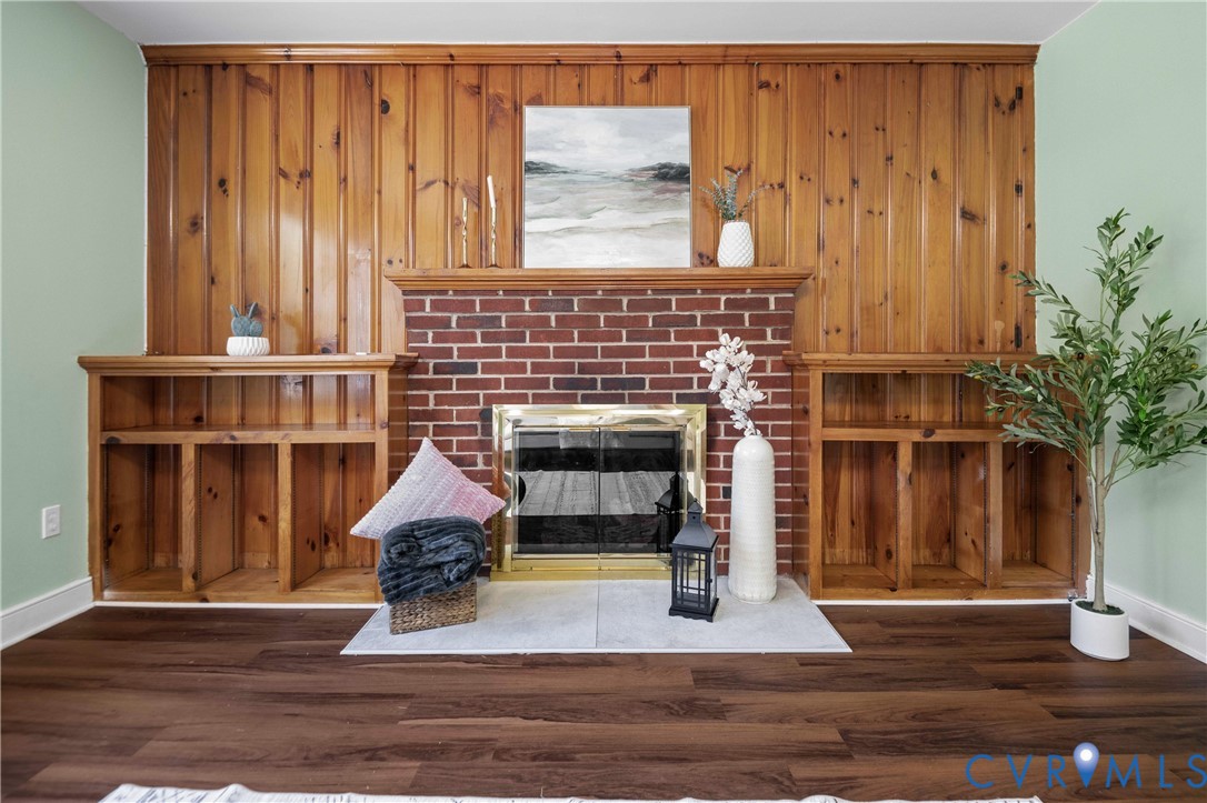 Floor-to-ceiling wood paneling, red brick fireplace, built-in shelving, stone hearth, and wood-finish flooring Floor-to-ceiling wood paneling, red brick fireplace, built-in shelving, stone hearth, and wood-finish flooring