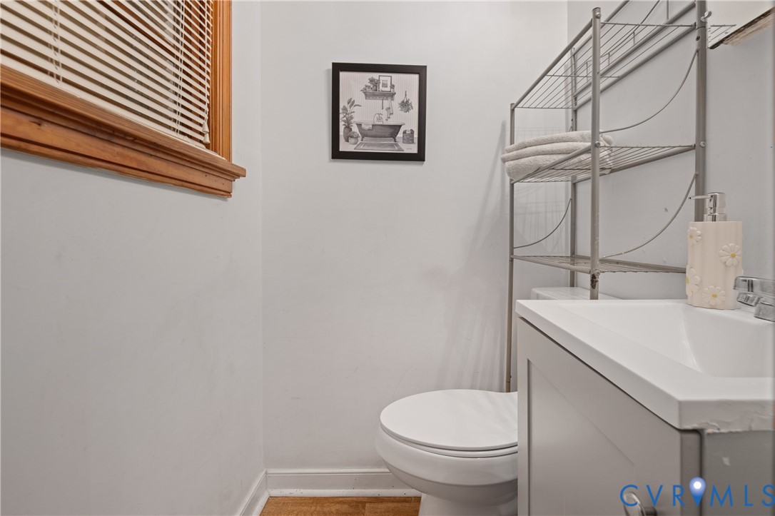 Bathroom featuring a grey vanity cabinet, integrated sink with a metallic faucet, wood-finish flooring, and a window with wood-tone blinds