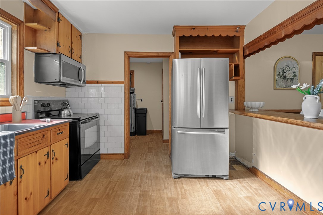 Kitchen featuring natural wood cabinetry, stainless steel refrigerator, built-in microwave, white subway tile backsplash, and wood-finish flooring