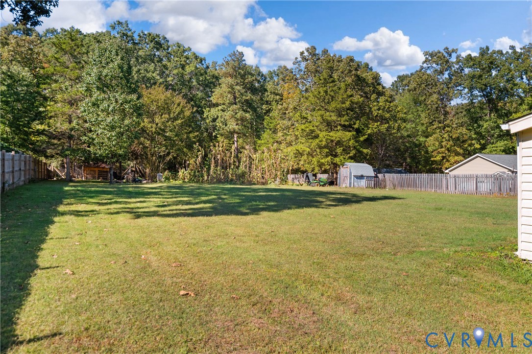 Expansive backyard featuring a large grass lawn, perimeter wooden privacy fencing, and dense mature tree line