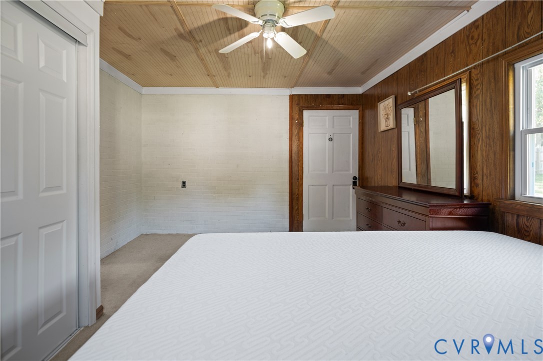 Beadboard ceiling with center-mounted ceiling fan, wood-paneled wall, white paneled doors, and multi-pane window
