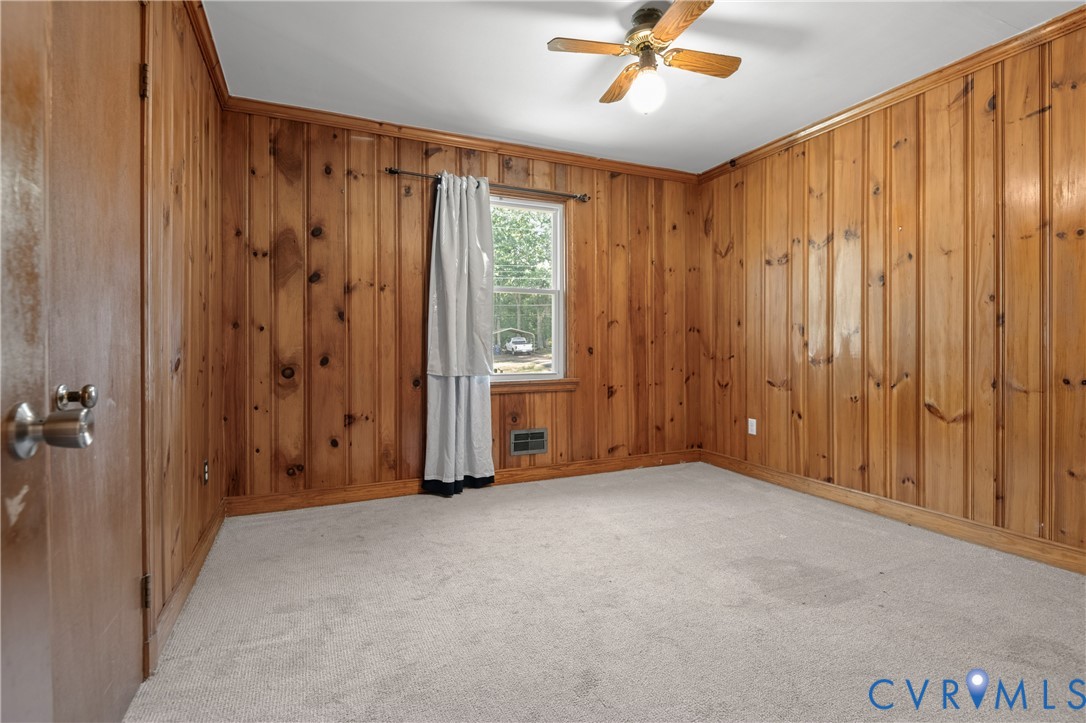 Room featuring natural wood-paneled walls, carpeted flooring, a single-hung window, and a central ceiling fan with an integrated light fixture