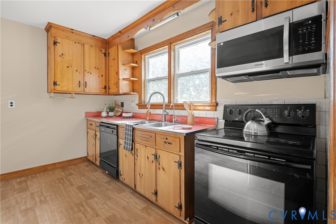 Kitchen featuring natural wood cabinetry, stainless steel appliances, double-basin sink, and wood-finish flooring