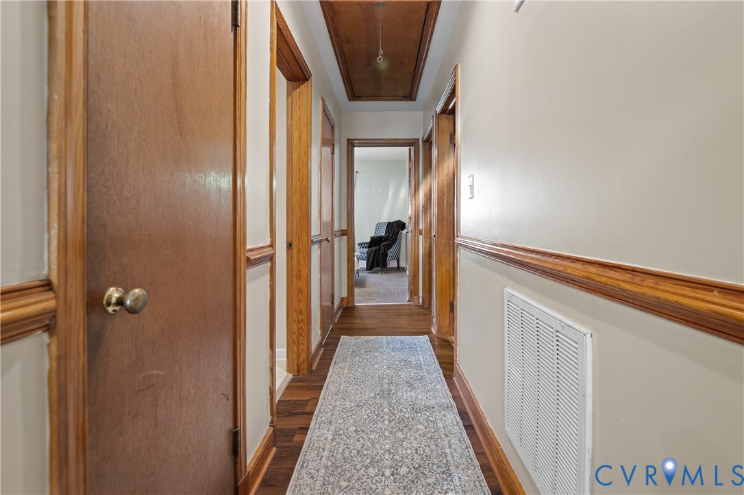 Interior hallway featuring wood-finish flooring, wood door trim and wainscoting, recessed ceiling paneling, and interior wood doors