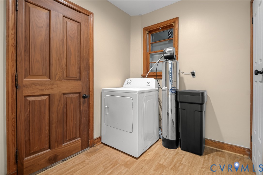 Utility area featuring a water softening system, wood-finish flooring, solid-core wood-style door, and a multi-pane window with wood trim