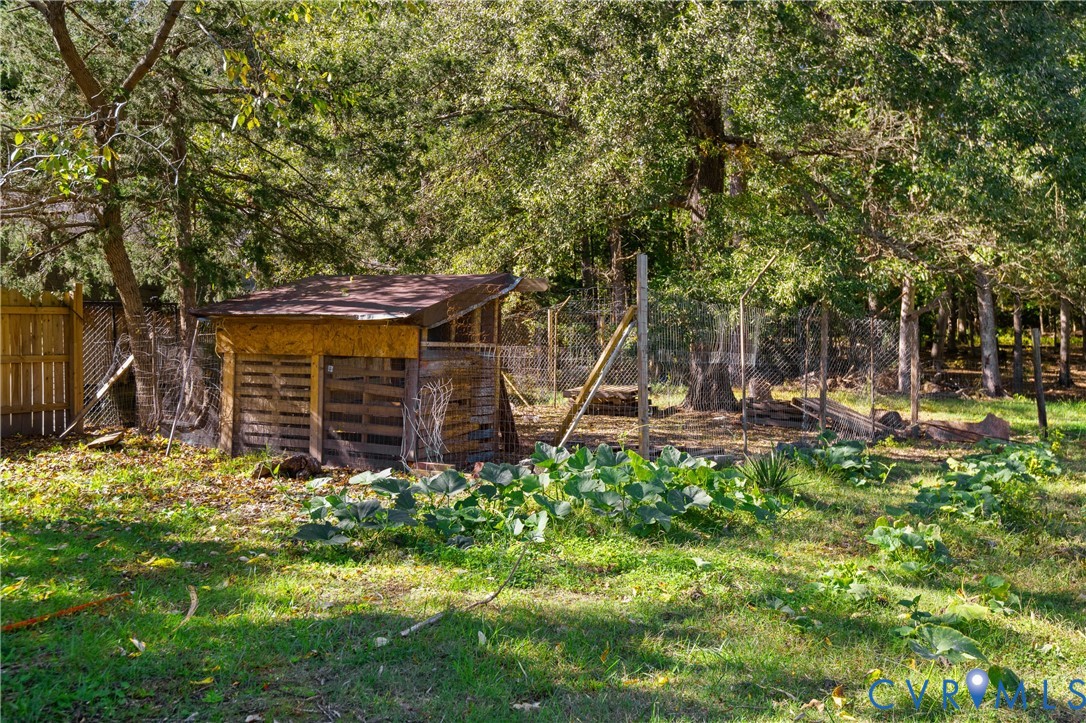 Outdoor structure with wood-slat siding, chain-link enclosure, and surrounding garden space set within a wooded lot