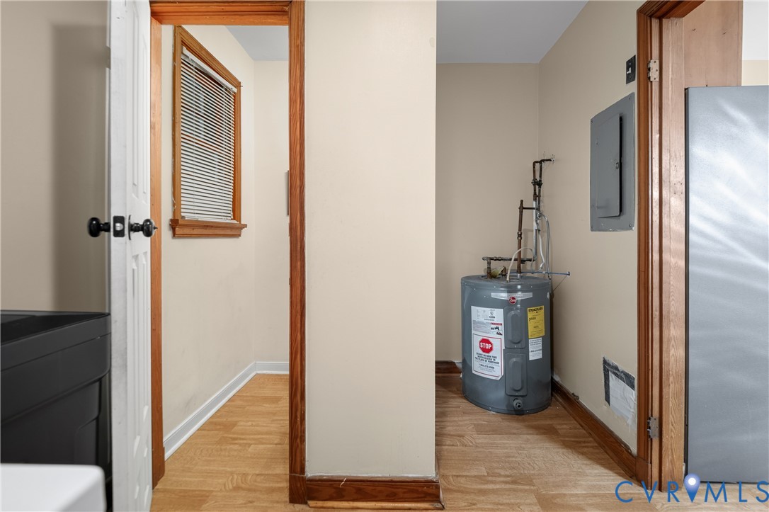 Utility area featuring wood-finish flooring, natural wood door casings, a recessed window with blinds, and a dedicated water heater