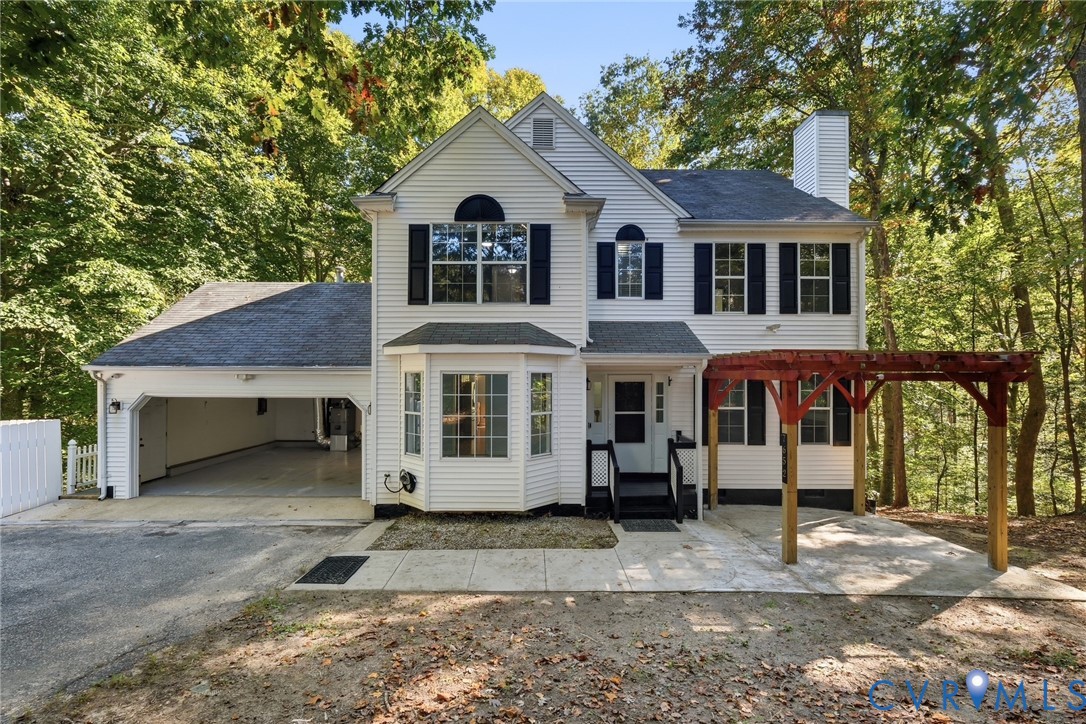 Two-story exterior featuring white vinyl siding, a multi-pane bay window, an attached two-car garage, and a timber-frame pergola Two-story exterior featuring white vinyl siding, a multi-pane bay window, an attached two-car garage, and a timber-frame pergola