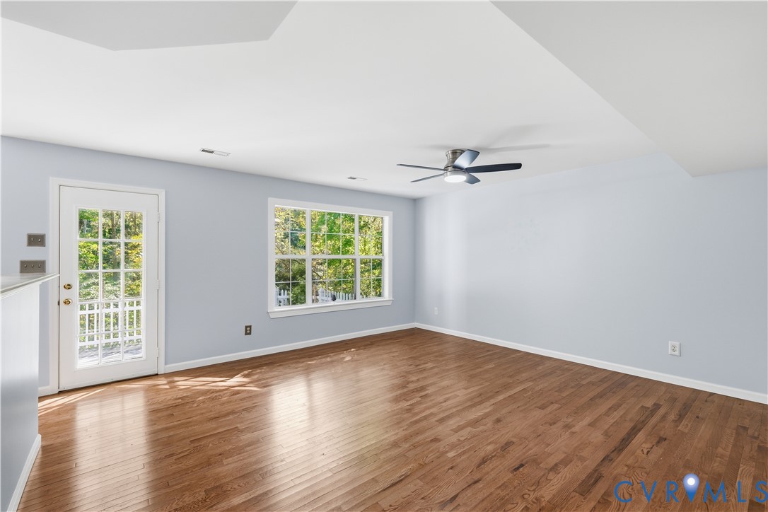 Spacious interior featuring wood-finish flooring, a multi-pane glass door, large picture window, and a ceiling-mounted light fixture with fan