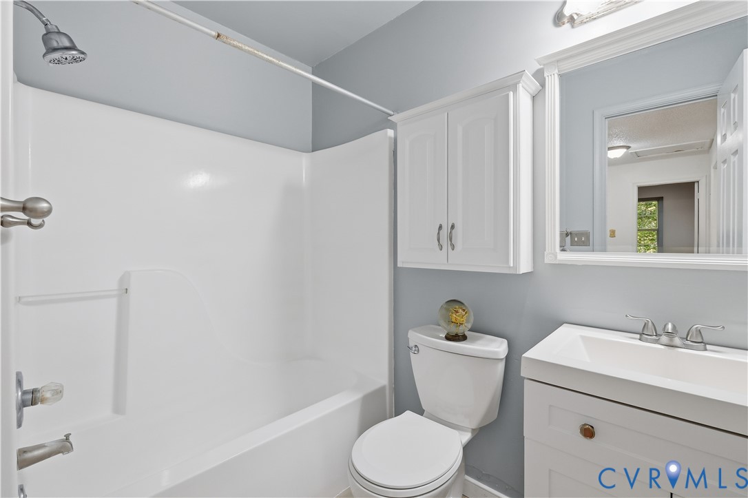 Bathroom featuring a white vanity cabinet with an integrated rectangular sink, a framed wall mirror, a white wall-mounted storage cabinet, and a bathtub with a white surround
