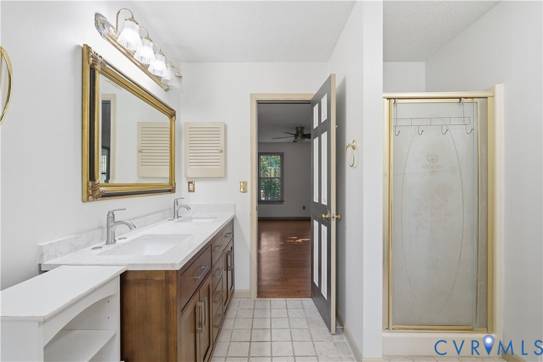 Double vanity with stone countertop, undermount sinks, wood-finish cabinetry, and glass-enclosed shower