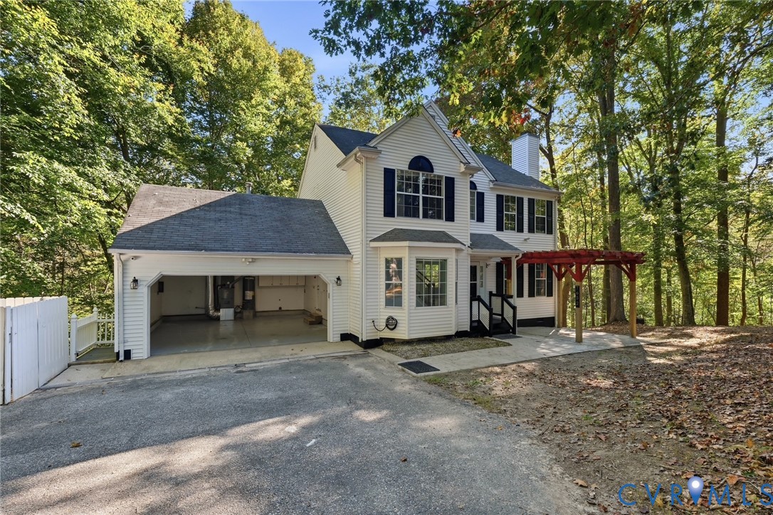 Two-story vinyl-sided exterior featuring an attached two-car garage, a wooden pergola, a bay window, and dark-finished shutters