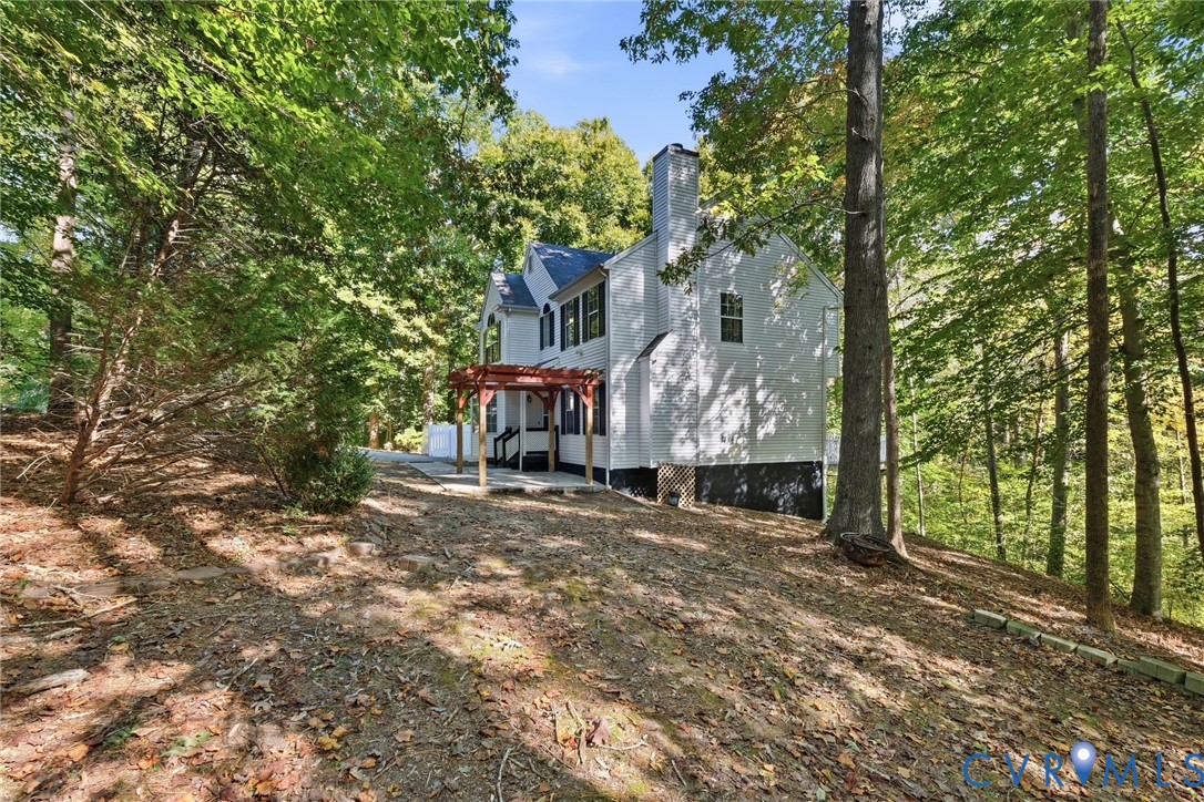 Two-story residence featuring a painted brick exterior, a wood-frame pergola, an attached chimney stack, and mature trees