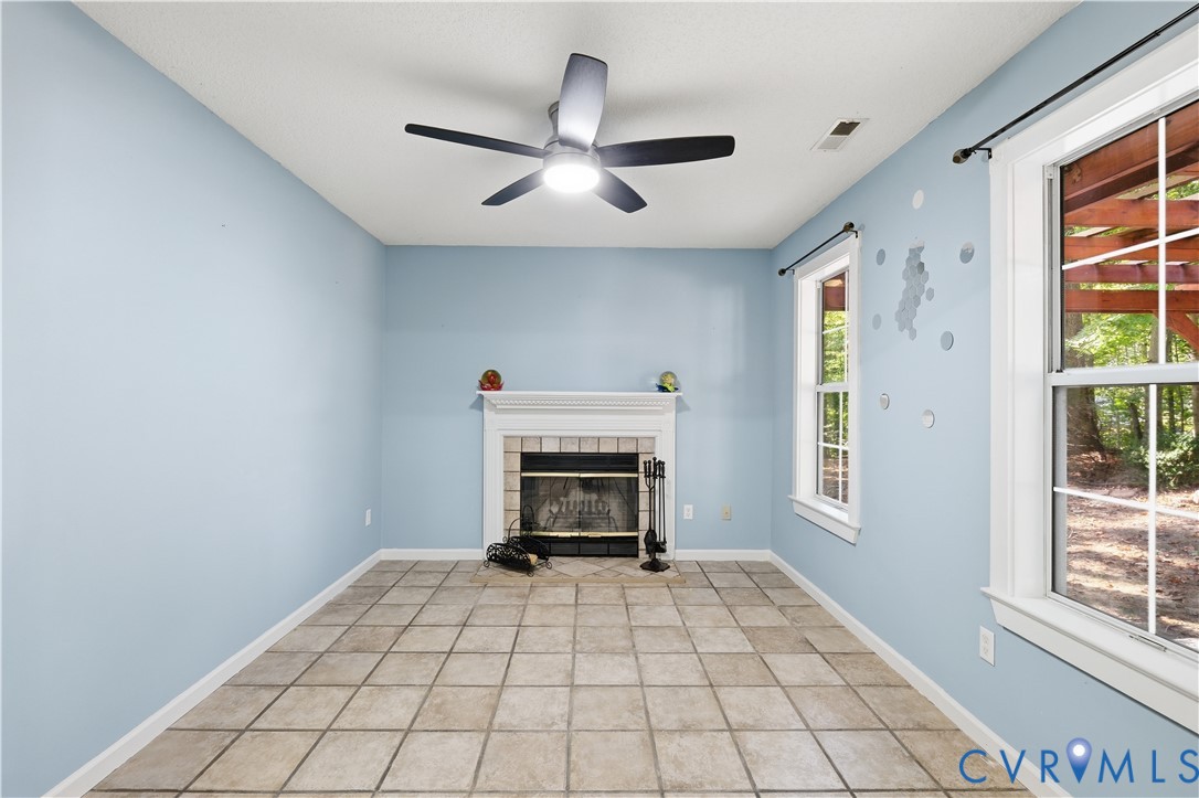 Fireplace with a white mantel and decorative tile surround, ceramic tile flooring, multi-blade ceiling fan with integrated light, and large windows with grid muntins