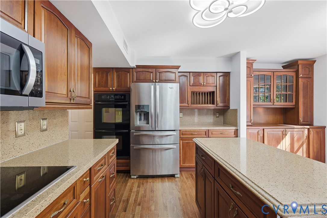 Kitchen featuring wood cabinetry, stone-style countertops, stainless steel appliances including a double wall oven, central island, and wood-finish flooring