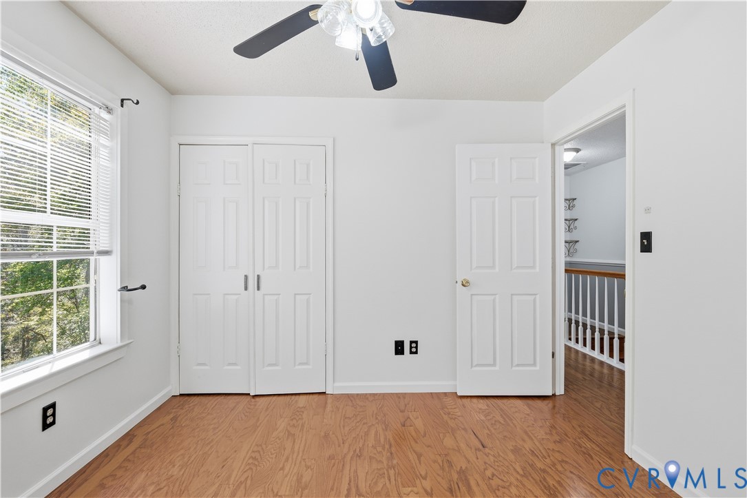 Room featuring wood-finish flooring, a multi-pane window with blinds, bi-fold closet doors, and a ceiling fan with integrated lighting