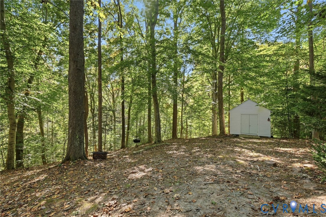 Expansive wooded lot featuring mature trees, a natural earth surface, and a detached white-sided storage structure with double doors