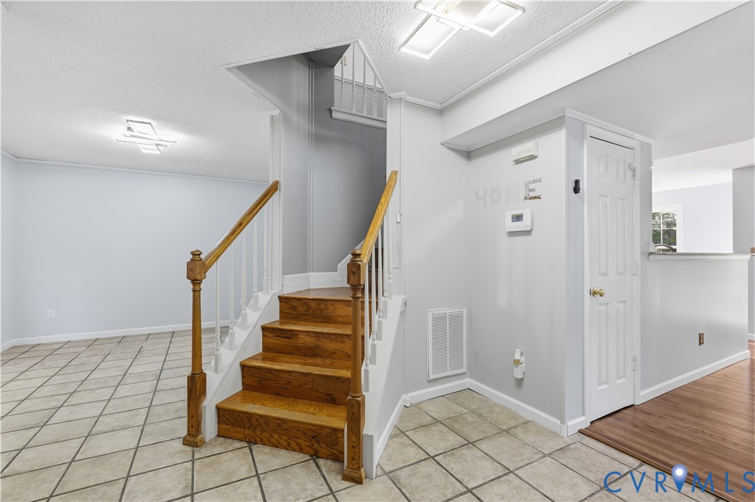 Staircase featuring wood treads, white balusters, and a finished wood newel post, complemented by neutral tile flooring and flush-mount lighting fixtures