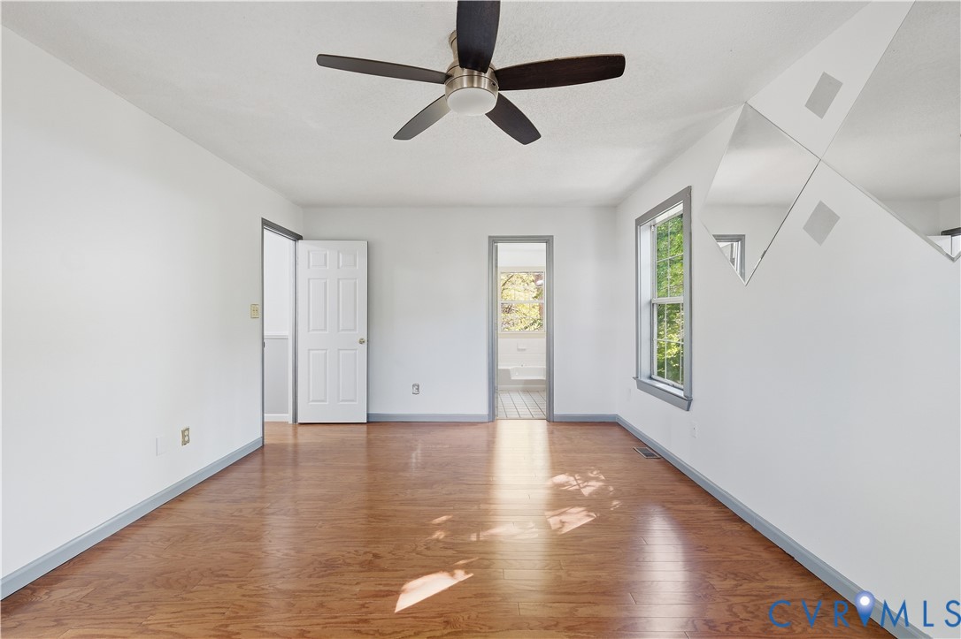 Wood-finish flooring, central ceiling fan with integrated lighting, diamond-patterned wall mirrors, and paneled interior door