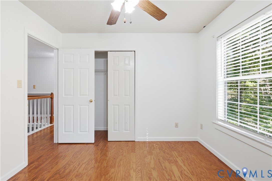 Room featuring wood-finish flooring, a double-door closet, a window with horizontal blinds, and a ceiling fan with integrated lighting