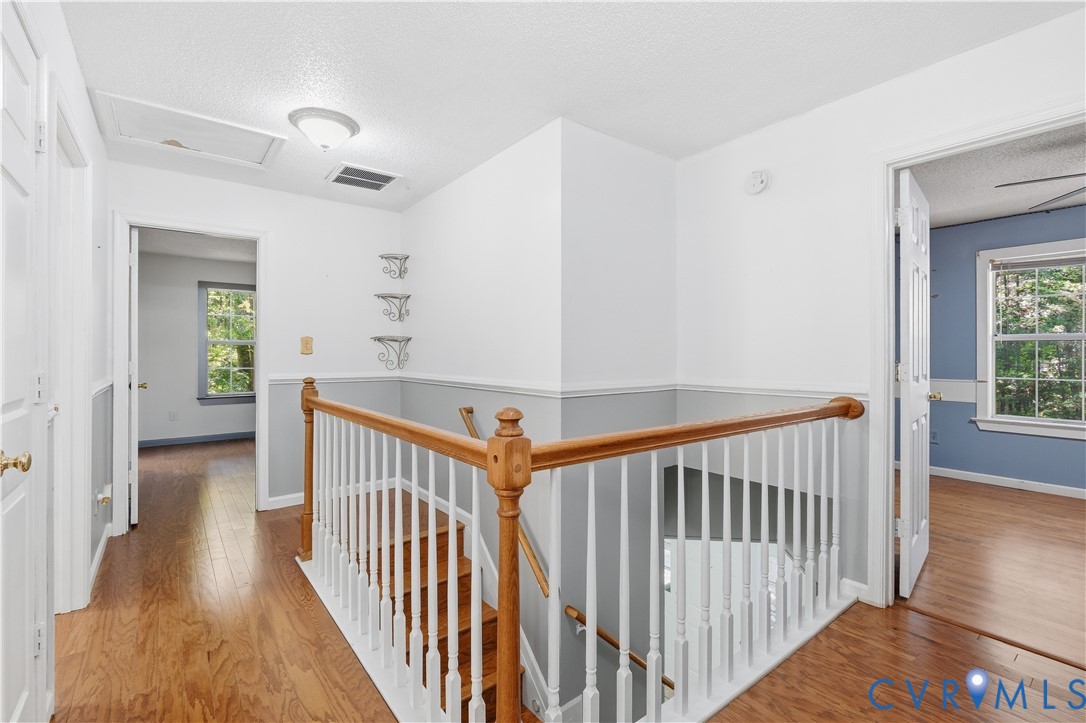 Landing area featuring wood-finish flooring, a traditional wood and white spindle railing, chair rail molding, and built-in wall shelving