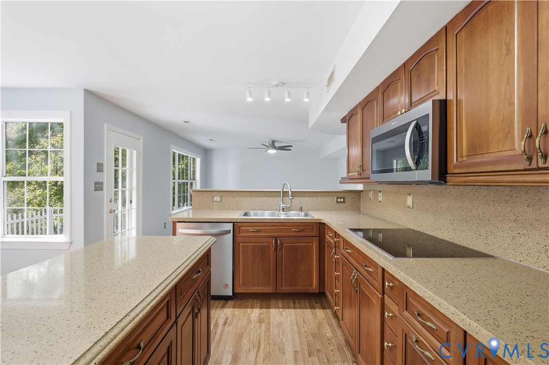 Kitchen featuring wood cabinetry, stone-composite countertops, stainless steel appliances, a peninsula, and wood-finish flooring