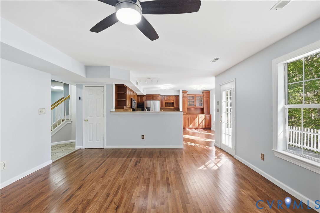 Wood-finish flooring, natural wood cabinetry, glass-paneled entry door, ceiling fan with integrated lighting, and multipane windows