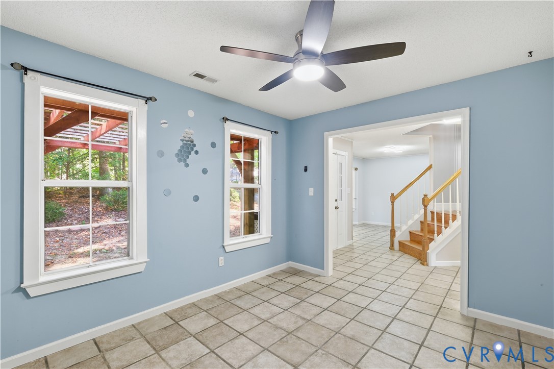 Tile flooring, multi-pane windows, ceiling fan with integrated lighting, and wooden staircase railing