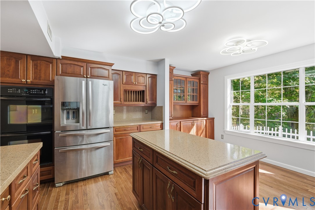 Kitchen featuring wood cabinetry, stone-surface countertops, central island, stainless steel refrigerator, and modern geometric ceiling fixtures