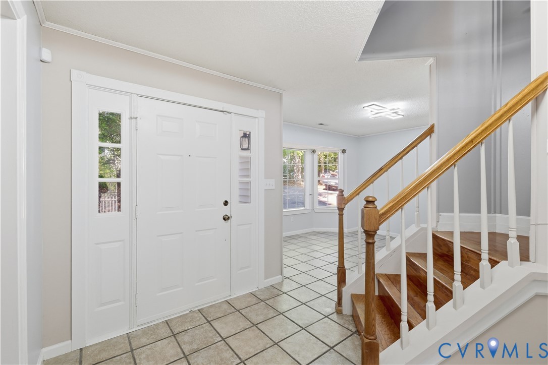 Entryway featuring tile flooring, staircase with wood-finish treads, decorative white balusters, and a paneled front door with glass sidelights
