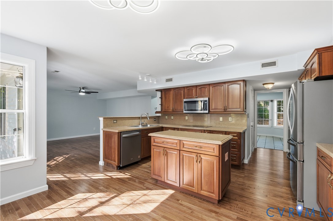Kitchen featuring wood cabinetry, stone-finish countertops, stainless steel appliances, a central island, and wood-finish flooring